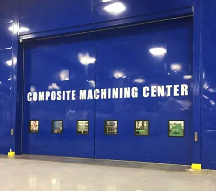 QuietSlide bi-parting oversized sliding acoustical door at a machining center. Royal blue with observation windows.