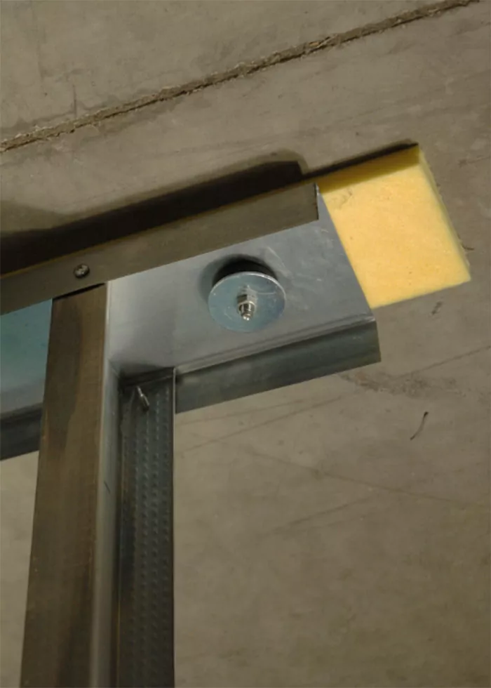 Field installation of Wallmat stud wall isolation pad with KAI bushing installed to a metal ceiling track.