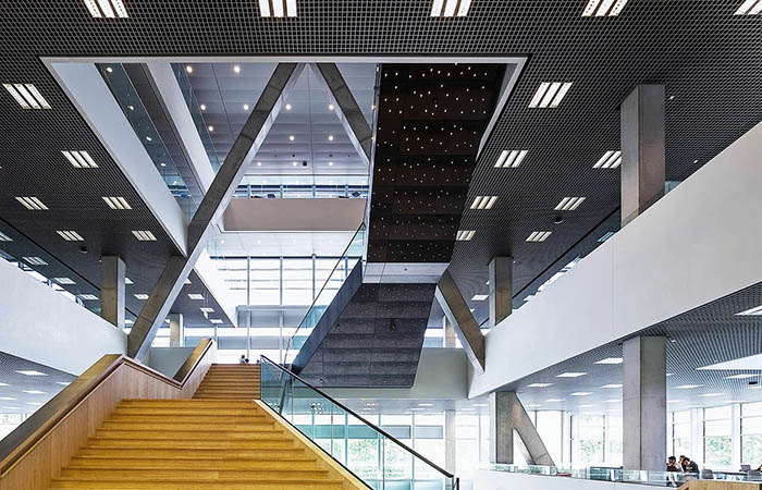 Square metal open cell ceilings in an open plan office with backlit metal staircase