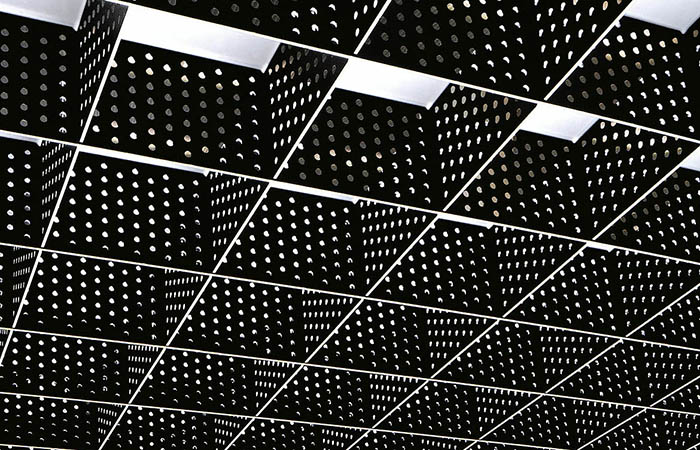 Detailed view of a perforated single blade rectangular metal open cell suspended ceiling in black coated finish