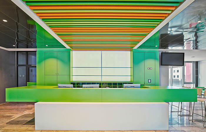 Orange and Green linear metal acoustical baffles with mirrored ceiling above a lobby desk.