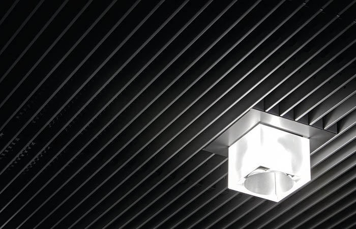 Detailed view of starlam linear open cell metal ceiling in black with lighting integration.