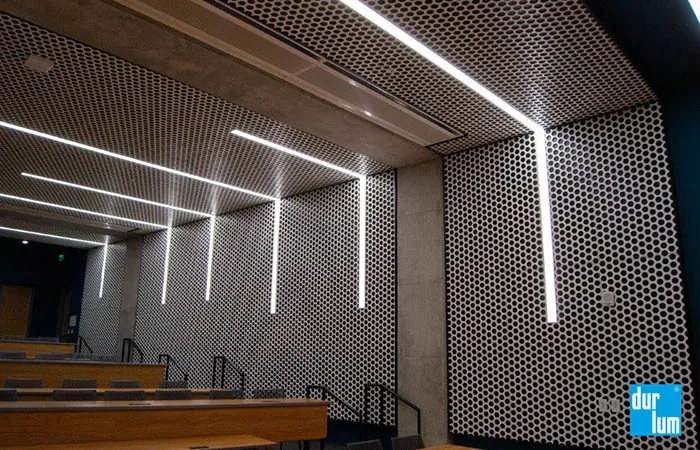 Loop metal ceiling and wall panels with linear light integration at a college auditorium classroom