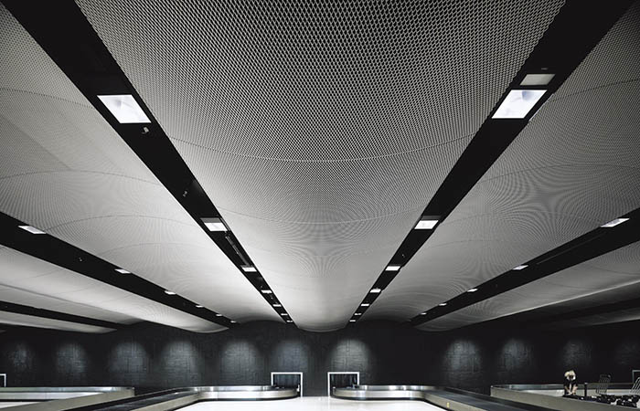 Sound absorbing expanded metal mesh ceiling with curved panels in an airport baggage claim.